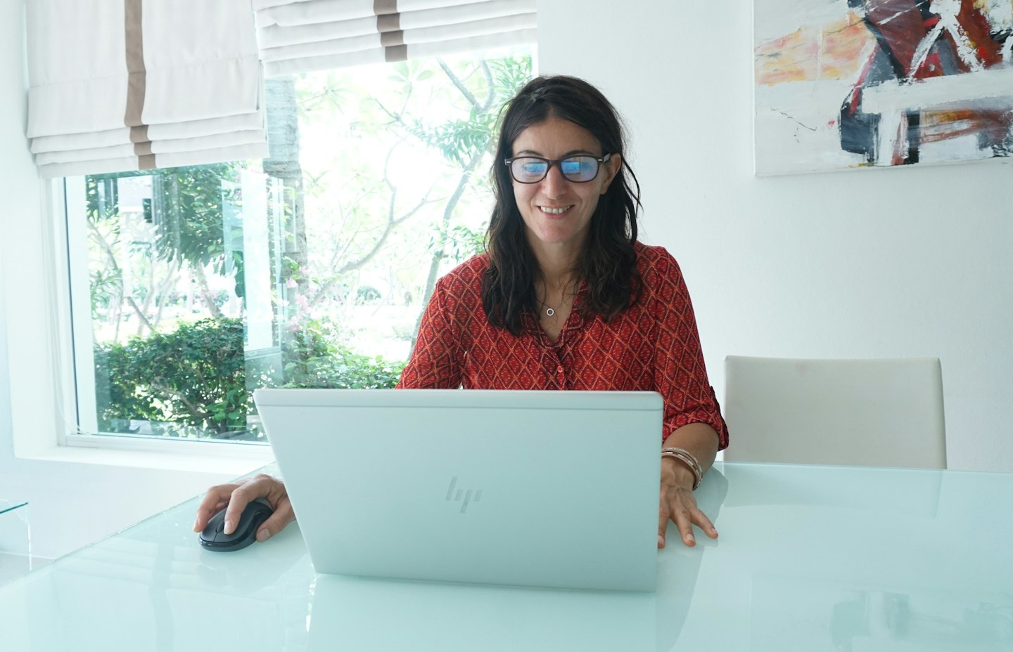 Woman in a red shirt works on her laptop at a desk.