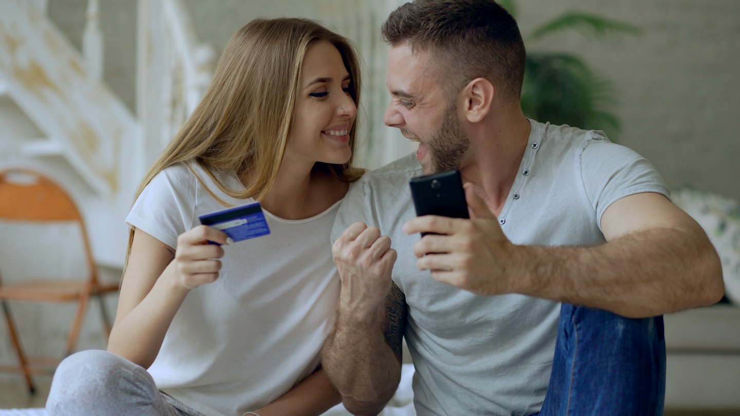 Couple excitedly looking at a smartphone with a credit card.